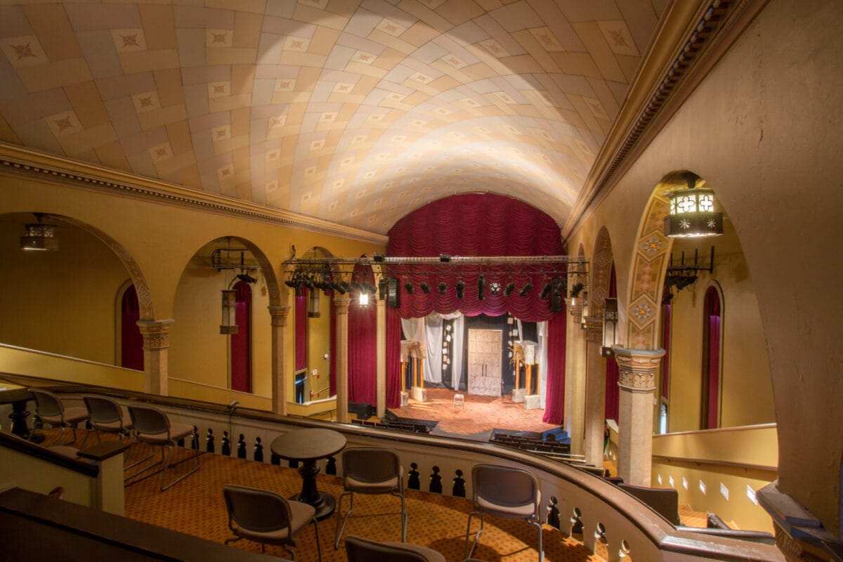 View of a vintage theater interior with arched ceiling, empty seats, and stage set for a performance.