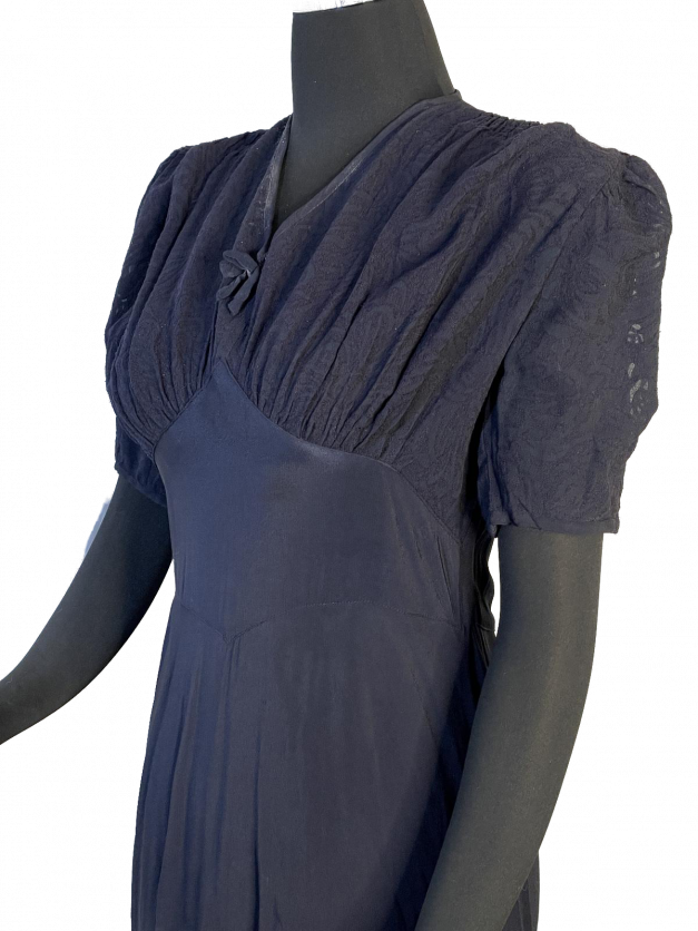 A Dainty Blue 1930s Vintage Dress drapes elegantly on a mannequin, its captivating hue resembling a deep blue ocean.