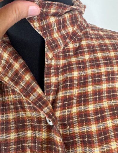 Hand holds brown plaid flannel 90s Levi's shirt with dagger collar on black mannequin, retro grunge style, medium size.
