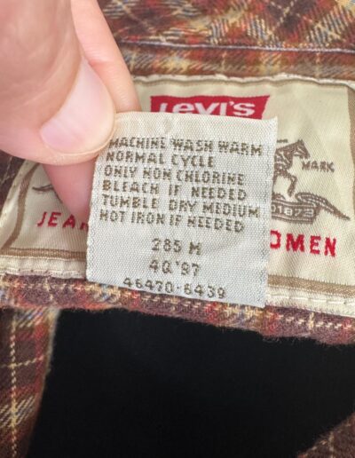 Hand holding care tag on a brown 90s Levi's plaid flannel shirt, showing Levi’s label and retro grunge button-down fabric.