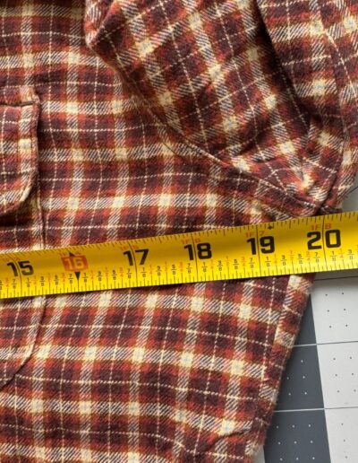 Vintage 90s Levi’s women’s medium plaid flannel shirt, yellow tape measuring 18" across sleeve on gray grid-patterned surface.