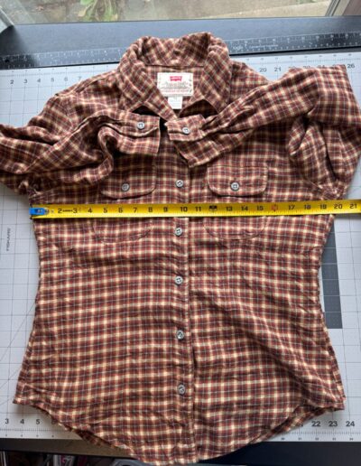 Brown vintage 90s Levi’s women’s plaid flannel shirt with dagger collar, flat on gridded mat, chest measured at 19 inches.