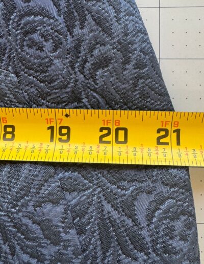 Yellow tape measure on navy blue floral brocade fabric, grid mat background, inspired by 1940s WWII midi dress style.