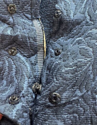 Hand holding 1940s navy blue floral brocade midi dress with mother of pearl buttons and WWII-era snap fasteners.