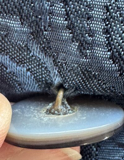 Close-up of fingers holding a mother of pearl button on 1940s handmade navy blue floral brocade midi dress with frayed buttonhole.