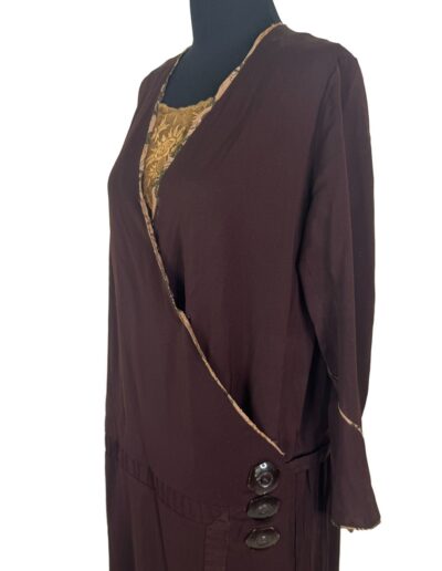 Plus size 1920s dark brown drop waist dress with Art Deco embroidery, long sleeves, side buttons, gold patterned neckline.