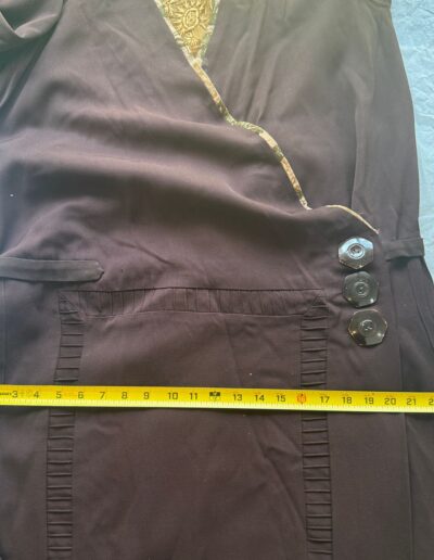 Plus size antique 1920s dark brown drop waist dress with Art Deco embroidery, wrap detail, and yellow measuring tape at waist.