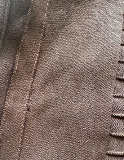 Dark brown Art Deco embroidered fabric from a plus size 1920s drop waist dress, showing textured seam, stitched pleats, and small hole.