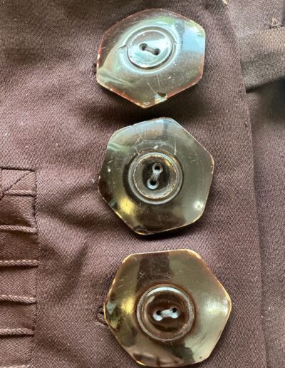Three dark hexagonal buttons on brown fabric with pleated stitching, antique 1920s Art Deco drop waist plus size dress detail.