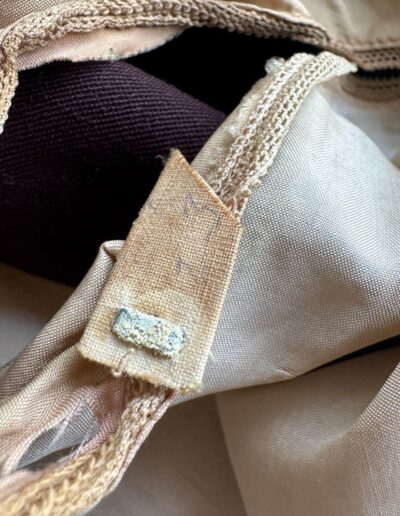 Off-white cloth tag with frayed edges and worn stitching on a dark brown 1920s Art Deco plus size drop waist dress.