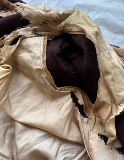 Close-up of torn underarm seam on plus size 1920s dark brown Art Deco drop waist dress with frayed beige fabric and exposed lining.