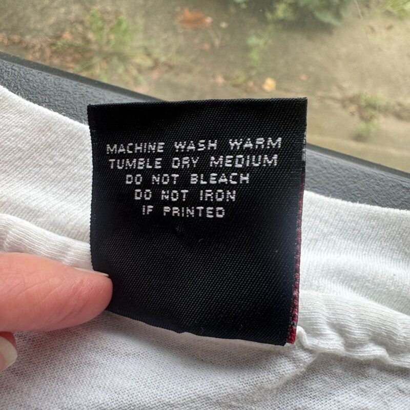 Hand holding a black cotton tag with white lettering on a vintage Def Leppard Seven Day Weekend Tour T-shirt.
