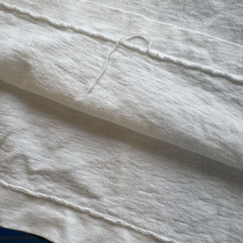 Close-up of white cotton fabric with visible stitching, loose thread, and vintage Def Leppard tour shirt details.