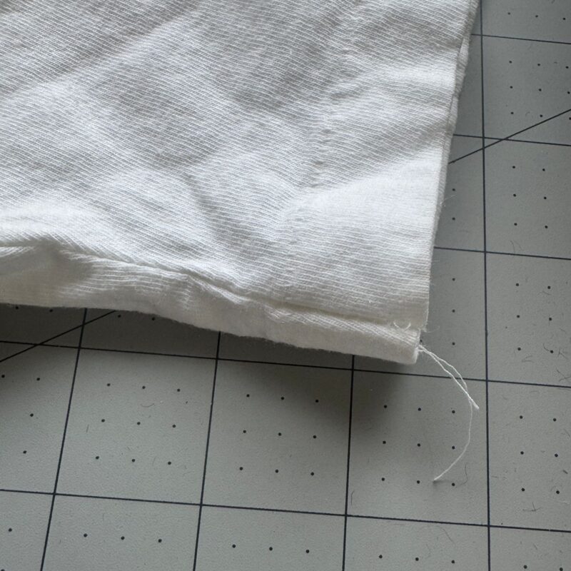 White cotton vintage Def Leppard T-shirt corner with loose thread on a gray grid-patterned surface.