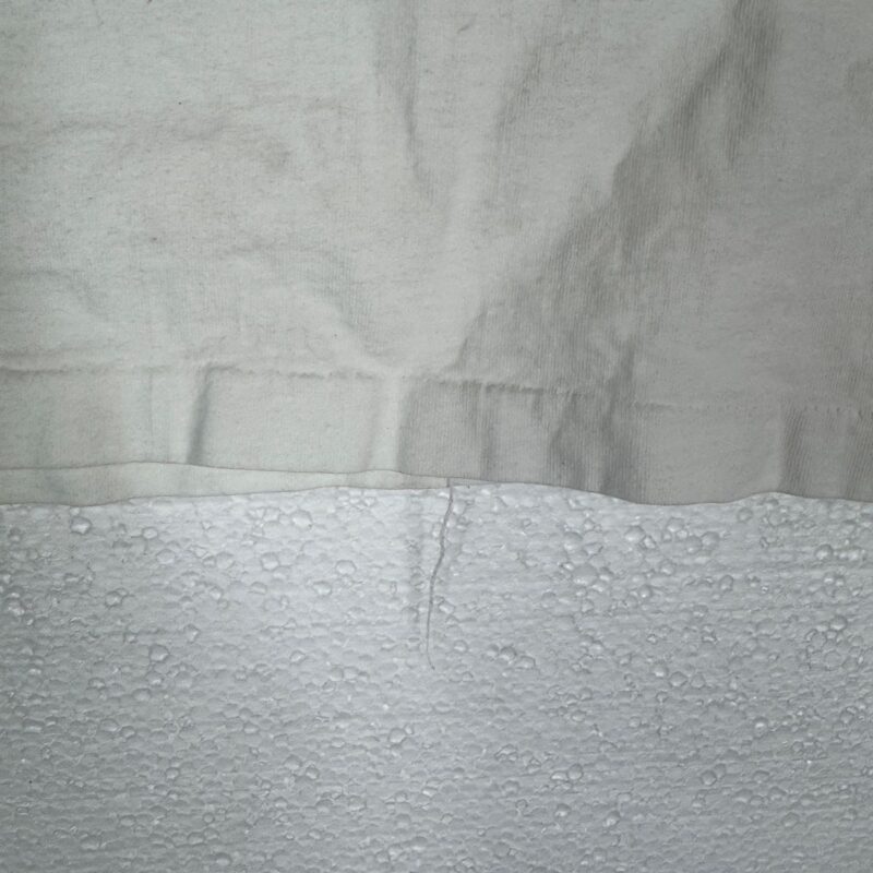 White cotton cloth with visible seam draped over bumpy white styrofoam, resembling vintage Def Leppard crew shirt material.