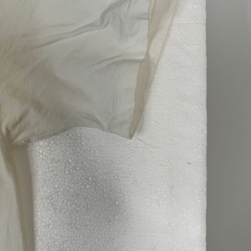 Thin off-white vintage Def Leppard shirt fabric over textured white foam, beside a smooth light gray wall.