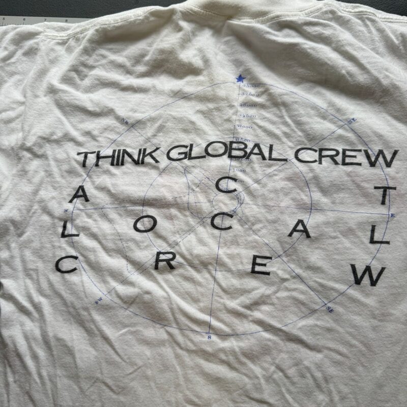 White vintage-style R.E.M. concert shirt with circular THINK GLOBAL CREW and LOCAL CREW text over a faint compass diagram.