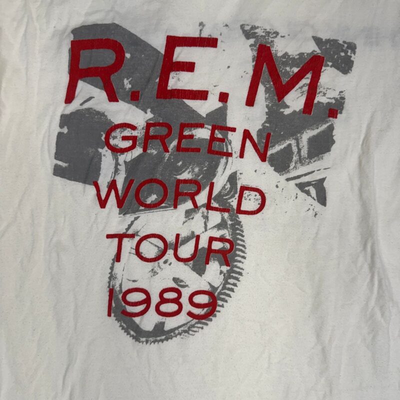 Vintage white cotton R.E.M. concert shirt with bold red tour text and faded gray abstract face graphic, 1989 style.