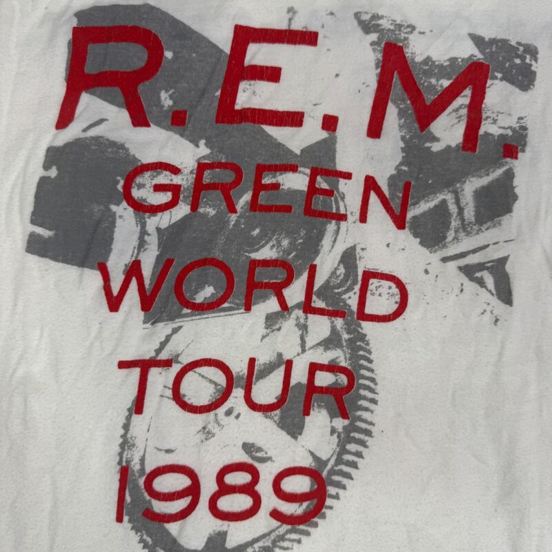 Vintage white cotton R.E.M. Green World Tour 1989 shirt with bold red text and a faded abstract gray graphic background.