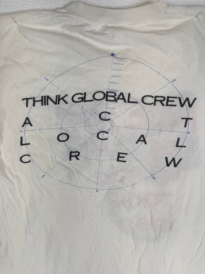 White cotton shirt with faint compass graphic, bold black THINK GLOBAL CREW ACT LOCAL CREW text, vintage R.E.M. Local Crew style.