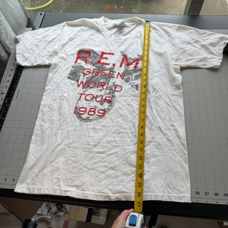 Black vintage R.E.M. Green World Tour 1989 concert shirt laid flat on cutting mat, tape measure showing shirt length.
