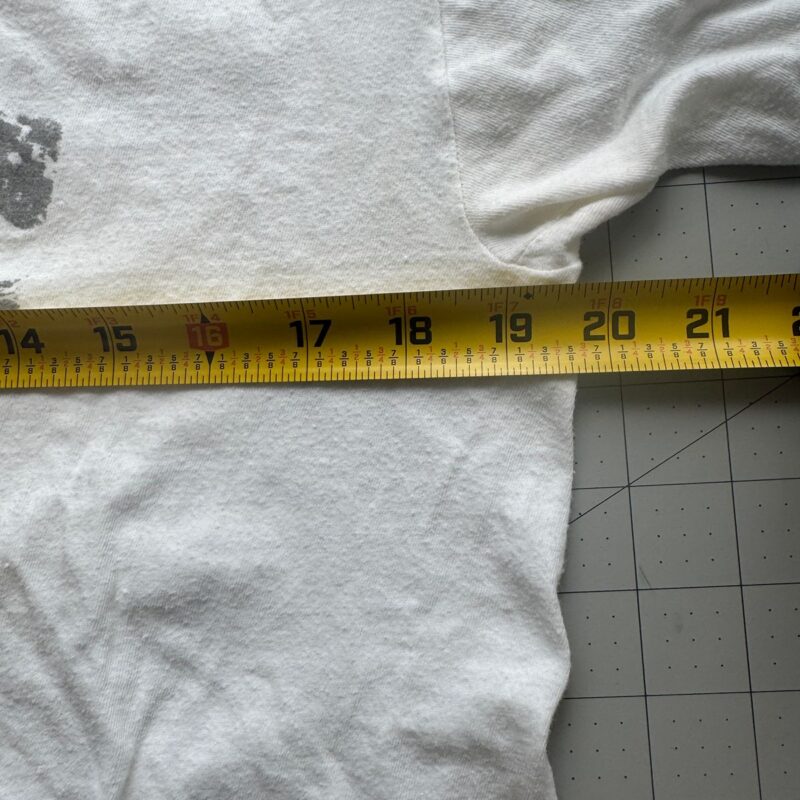 Yellow tape measure across vintage black R.E.M. band T-shirt, 20-inch chest width, on gray grid cutting mat.