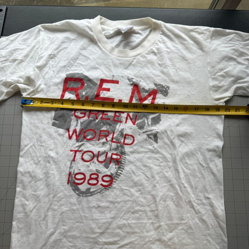 White vintage R.E.M. Green World Tour 1989 T-shirt laid flat, yellow tape measure across chest, classic rock concert tee.