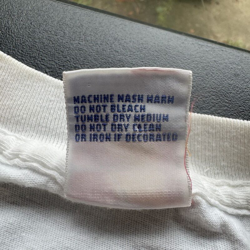 White cotton vintage R.E.M. concert shirt from 1989 with a blue-text care label attached; St. Louis event collectible.