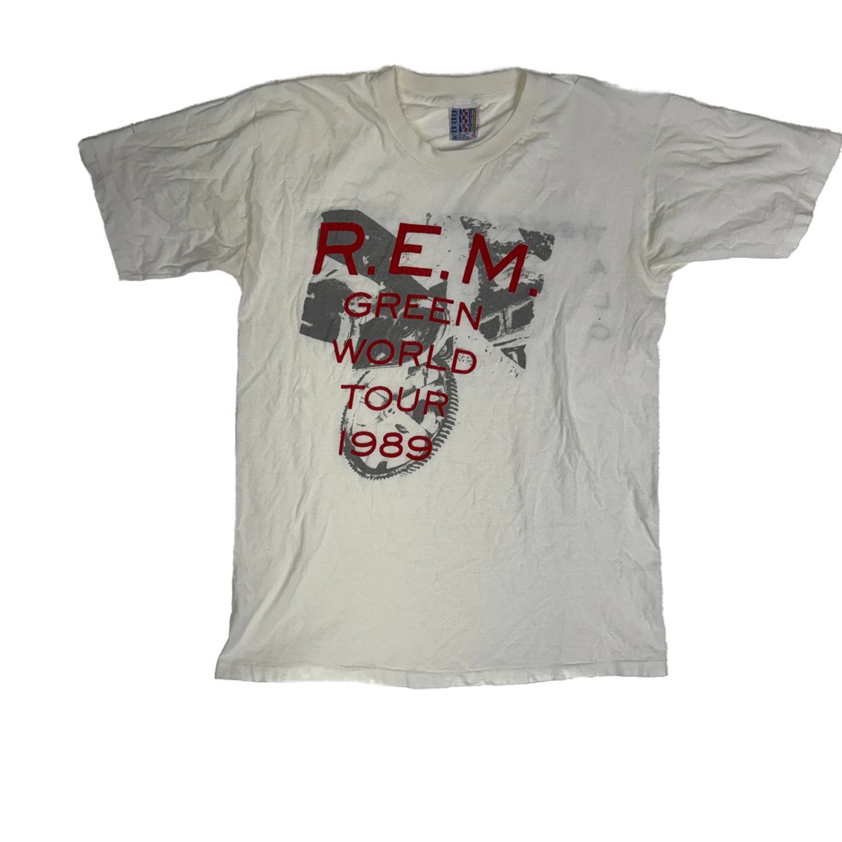 White vintage R.E.M. T-shirt, red and gray “R.E.M. Green World Tour 1989” text, faded graphic, worn cotton 1989 tour shirt. White vintage R.E.M. T-shirt, red and gray “R.E.M. Green World Tour 1989” text, faded graphic, worn cotton 1989 tour shirt.