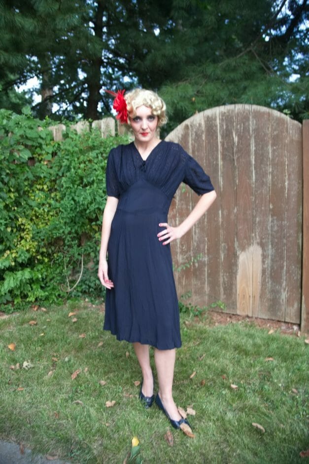 A woman in a Dainty Blue 1930s Vintage Dress posing in front of a fence from the 1930s.