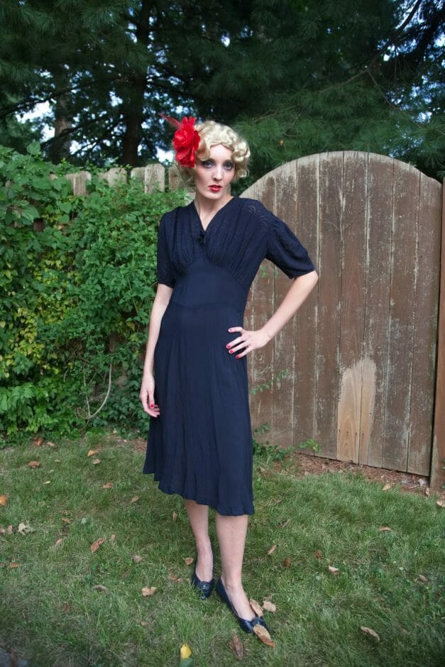 A woman in a Dainty Blue 1930s vintage dress with a red flower on her head.
