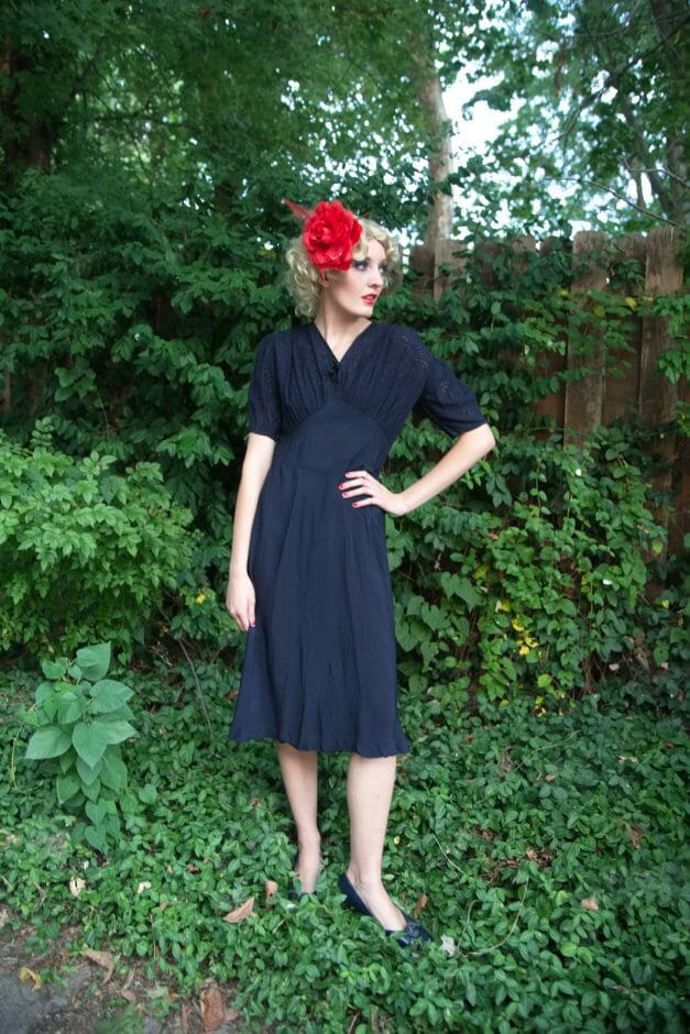 A woman in a Dainty Blue 1930s Vintage Dress with a red flower on her head.