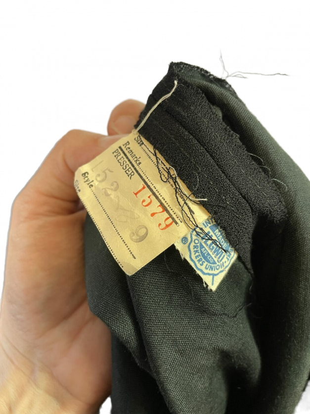 A person holding a Sexy little black dress vintage 1950s sheath with a label on it, available for sale.